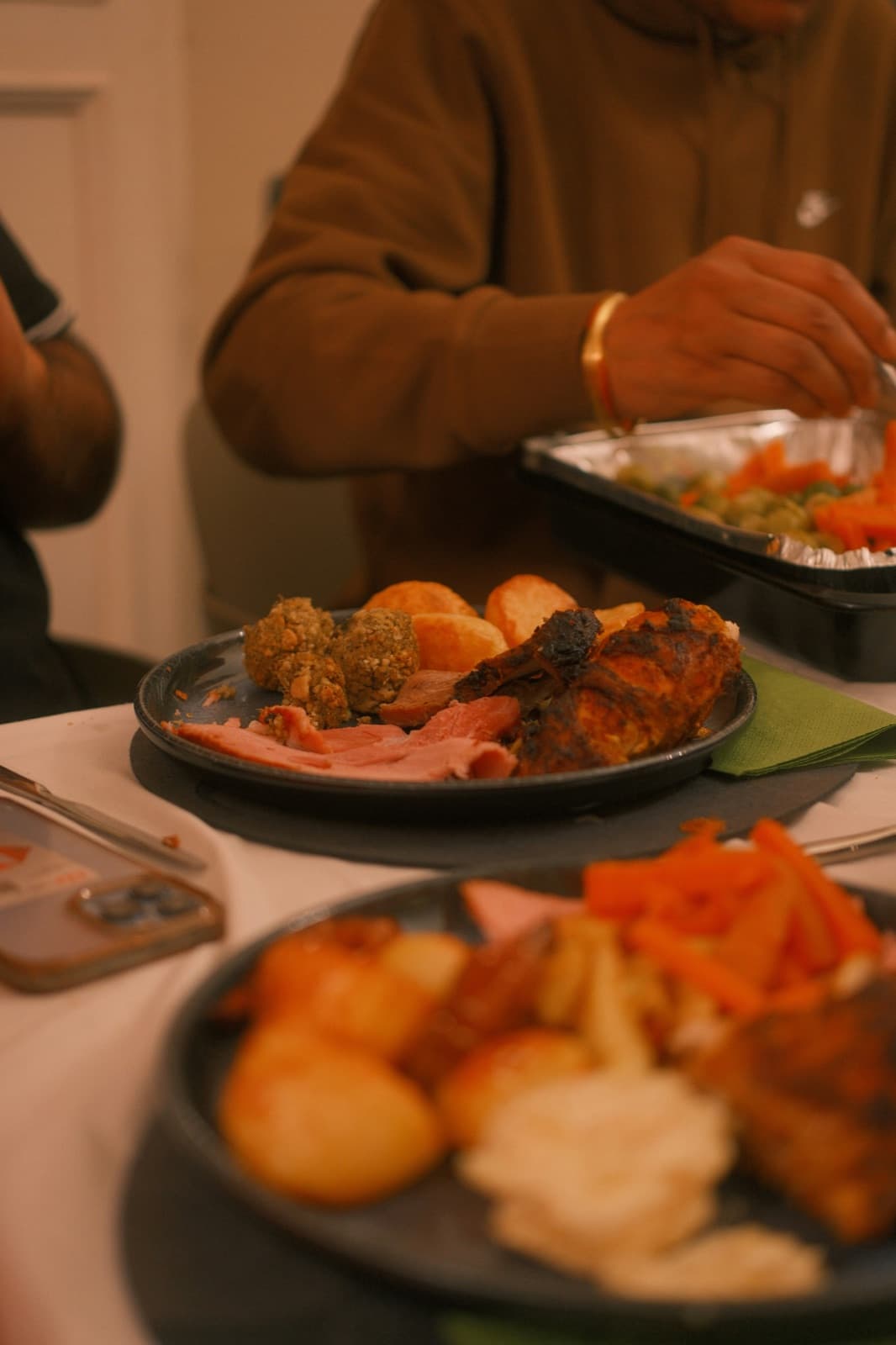 Plates of roast dinner on a table, ham, chicken, potatoes and stuffing, with someone serving from a tray behind