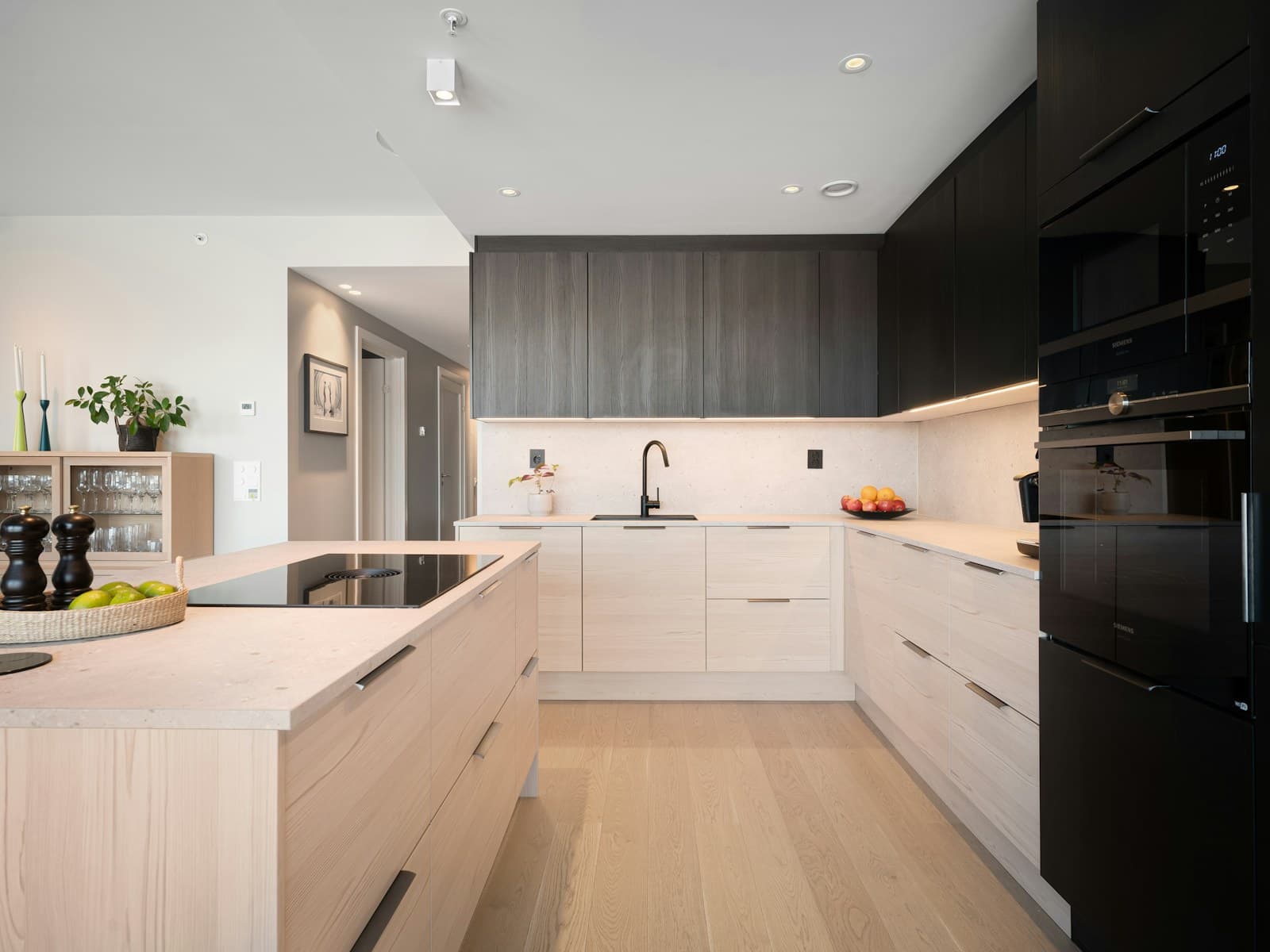 A kitchen with a pale stone island, dark upper joinery and a window seat beyond